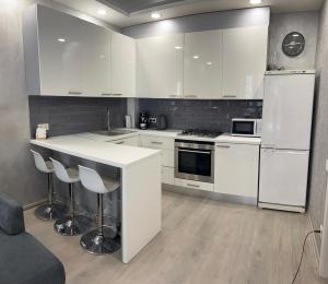 a kitchen with white cabinets and a counter with stools at Сучасна та простора квартира в гарному районі міста біля парку in Irpin'