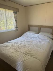 a large white bed in a bedroom with a window at Great Caravan At Dovercourt Holiday Park, Essex Ref 44206V in Great Oakley