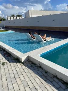 two people sitting in chairs in a swimming pool at Casa em Parnaíba 6km praia in Parnaíba