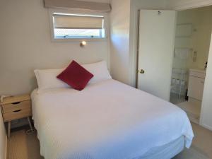 a bedroom with a white bed with a red pillow on it at Private Self Contained Unit Dog Friendly in Claudelands
