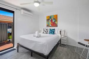 a white bedroom with a bed and a balcony at Cosy Hideaway Studio - Close to Everything in Buddina +5 photos