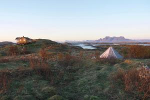 a tent in a field with a lake and a house at Helligvær Kystopplevelser AS in Helligvær +19 photos