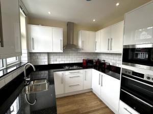 a kitchen with white cabinets and black appliances at Stunning South Croydon Apartment - Relax in Style in Purley