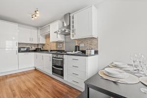 a kitchen with white cabinets and a table with plates at Stylish 4 Bedroom House in St Neots w Free Parking in Saint Neots