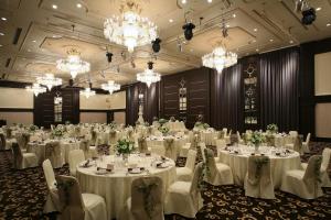 un salón de banquetes con mesas y sillas blancas y lámparas de araña en Hotel Green Tower Makuhari, en Chiba