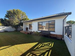 a white house with a bench in a yard at Barking Beach Cottage, Sandbaai - Pet Friendly in Hermanus