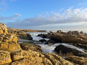 a rocky shoreline with the ocean and the waves at Barking Beach Cottage, Sandbaai - Pet Friendly in Hermanus +10 photos
