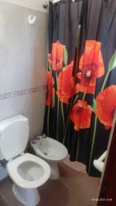 a bathroom with a toilet and a shower curtain with red flowers at Posada del Arroyo in Las Rabonas