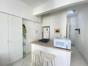 a kitchen with a counter with a microwave and stools at Conforto perto do Mar em São Vicente! in São Vicente
