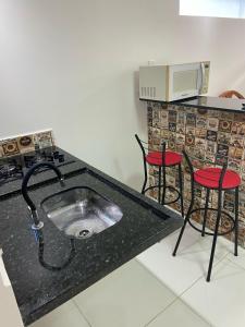 卡波布里奥Studio no Condomínio dos Pássaros em Cabo Frio e Belas Praias的厨房配有水槽和2把红色椅子