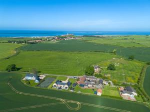 an aerial view of a house in a field with the ocean at Barn Cottage - North East Escapes in Bamburgh