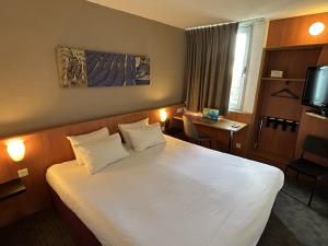 a hotel room with a large white bed and a table at Kyriad Martigues Sud in Martigues