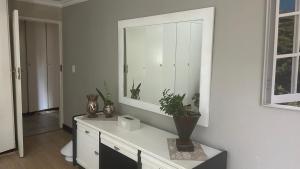 Cette chambre blanche dispose d'un miroir et d'une table avec des plantes. dans l'établissement Artzys Cottage 1km to Olivedale Clinic, à Northriding 21 autres photos