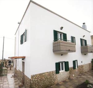 マテーラにあるCasale Delle Pianeの緑の窓とバルコニーが備わる白い建物