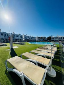 a row of chaise lounges on the grass near a swimming pool at Bungalow Simone in Maspalomas +16 photos