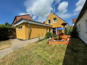 a yellow house with a playground in the yard at Das Melkmanns in Garding