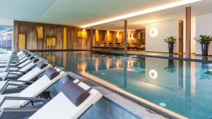 - une grande piscine avec des chaises blanches dans un bâtiment dans l'établissement La Casies Mountain Living Hotel, à Santa Maddalena in Casies