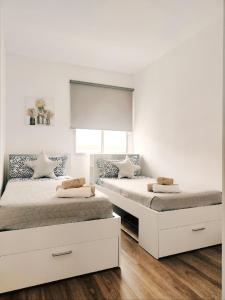 two beds in a bedroom with white walls and wood floors at Escapada Deluxe con Wifi 2 Hab 2 Baños con Cocina & SmartTV cerca de Todo in Santa Cruz de Tenerife
