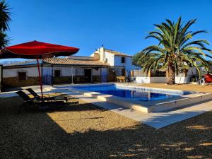 a swimming pool with a red umbrella and a chair and a house at Casita-Max 7Guests-Private Pool-Patio-Bbq-Parking in Las Norias