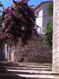 un bâtiment avec des fleurs violettes sur un mur en pierre dans l'établissement Central Studio Apartments & Dormitory Rooms, à Supetar