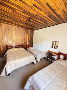three beds in a room with wooden ceilings at Pousada Pinheiro Real in Campos do Jordão