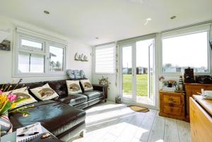 a living room with a leather couch and windows at The Happy Hedgehog in Mundesley