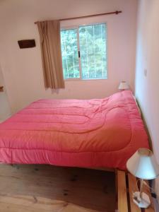 Cette chambre dispose d'un lit avec une couette rouge et d'une fenêtre. dans l'établissement CABAÑA PRIVADA NALÚ 2, Villa Ciudad Parque a 150m Río Los Reartes, à Villa Ciudad Parque 16 autres photos