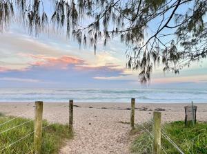 a sandy beach with a fence and the ocean at Korora's Haven Coffs Harbour in Kororo Basin