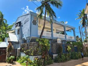 a blue house with a balcony and palm trees at Studio Poivre - Séjour tropical à Nosy Be in Madirokely