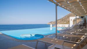 a swimming pool with chairs and the ocean in the background at Rocks and Waves Sifnos in Kamares