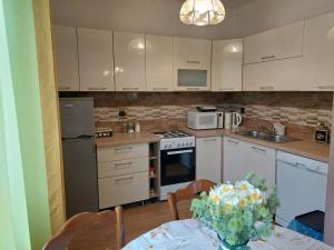 a kitchen with white cabinets and a table with a vase of flowers at Apartman Rozmari in Lokve