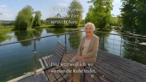Eine ältere Frau auf einer Bank neben einem Fluss. in der Unterkunft FeWo Lüneburger Heide - Minni in Bad Bevensen