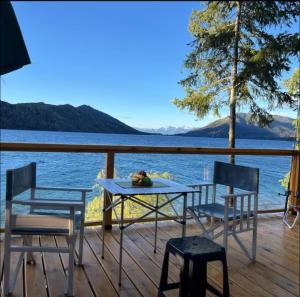 a table and chairs on a deck with a view of the water at Cabaña sobre Playa Lago Gutierrez 1 in San Carlos de Bariloche
