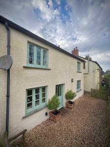 ein weißes Haus mit zwei Fenstern und zwei Topfpflanzen in der Unterkunft Old church cottage in Chulmleigh