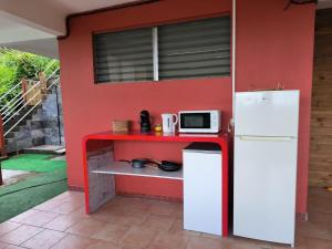 a small kitchen with a red wall with a white refrigerator at studio Caraïbes in Les Trois-Îlets