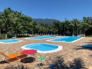 a group of three swimming pools with chairs and palm trees at Chácara Recanto Paraíso das Águas in Morretes