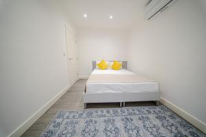 Dormitorio blanco con cama con almohadas amarillas y alfombra en Ilford Luxury Apartments, en Ilford