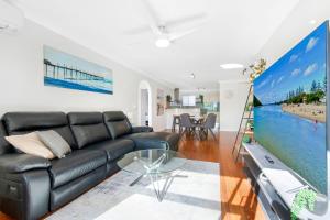 a living room with a black leather couch and a tv at Hawaiian Gardens 17 in Coffs Harbour
