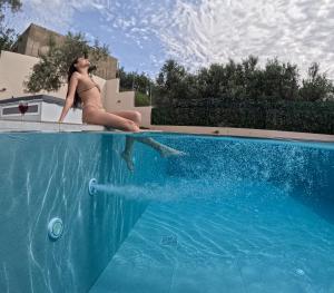 Eine Frau im Bikini sitzt am Rand eines Schwimmbeckens in der Unterkunft Villa Daratso with private heated pool view to the sea in Daratso