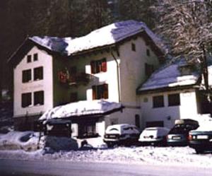 a snow covered house with cars parked in front of it at Hotel Cristallina in Sils Maria