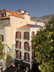 an apartment building with red shutters and a tree at Safira Suites 101 in Funchal