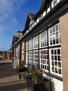 um edifício preto e branco com um banco à frente em The Panmure Arms Hotel em Edzell