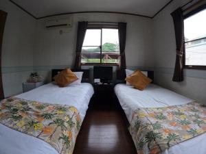 two beds in a room with a desk and two windows at ao とかしくビーチサイド in Tokashiki