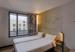 two beds in a hotel room with a window at B&B HOTEL Bordeaux Bassins à flot in Bordeaux