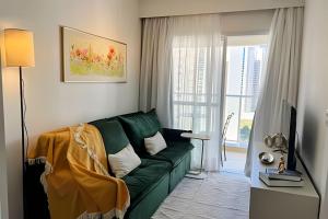 Una sala de estar con un sofá verde y una ventana. en Apto charmoso Gleba Palhano, en Londrina