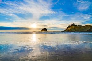 a beach with the sun shining on the water at Cape Kiwanda Hideaway in Pacific City