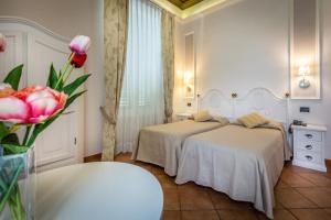a bedroom with two beds and a vase of pink flowers at Hotel Ferrucci in Florence