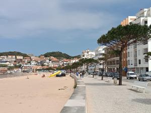 a beach with buildings and people walking on the sand at Baia Carmona in São Martinho do Porto