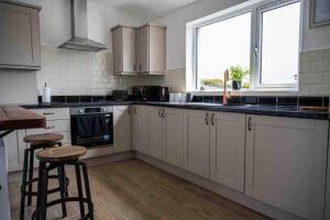 eine Küche mit weißen Schränken und 2 Barhockern in der Unterkunft Roddys cottage three bedroom with hot tub sleeps6 in Magherasaul