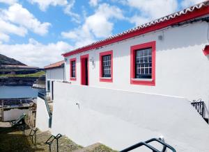 a white building with red windows and a body of water at Casa do Beco in Angra do Heroísmo